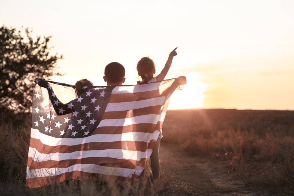 Two children holding an American flag at sunset.