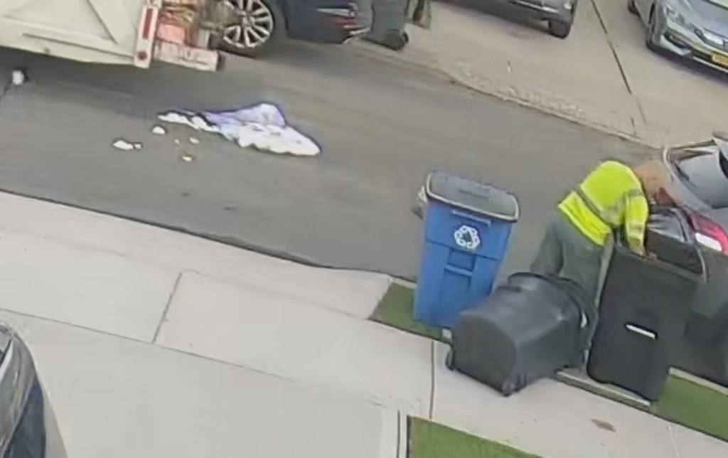 Garbage truck and a sanitation worker next to garbage cans on a street.