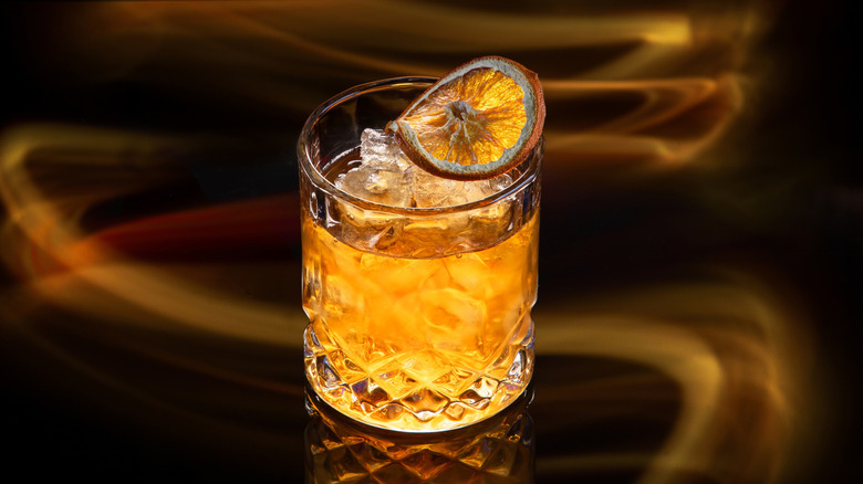 A Manhattan cocktail on the rocks in a glass tumbler, garnished with an orange