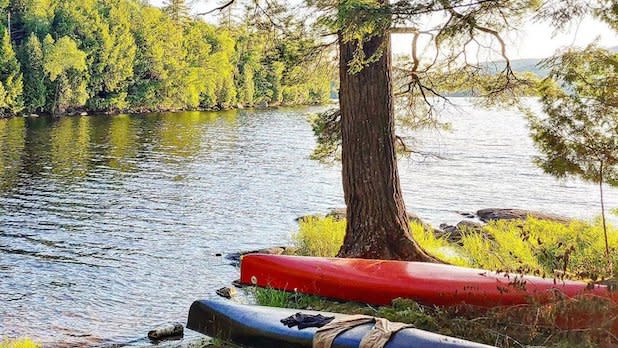 a red and a blue kayak sit on the edge of an island with Saranac Lake and the Adirondack woods as a backdrop