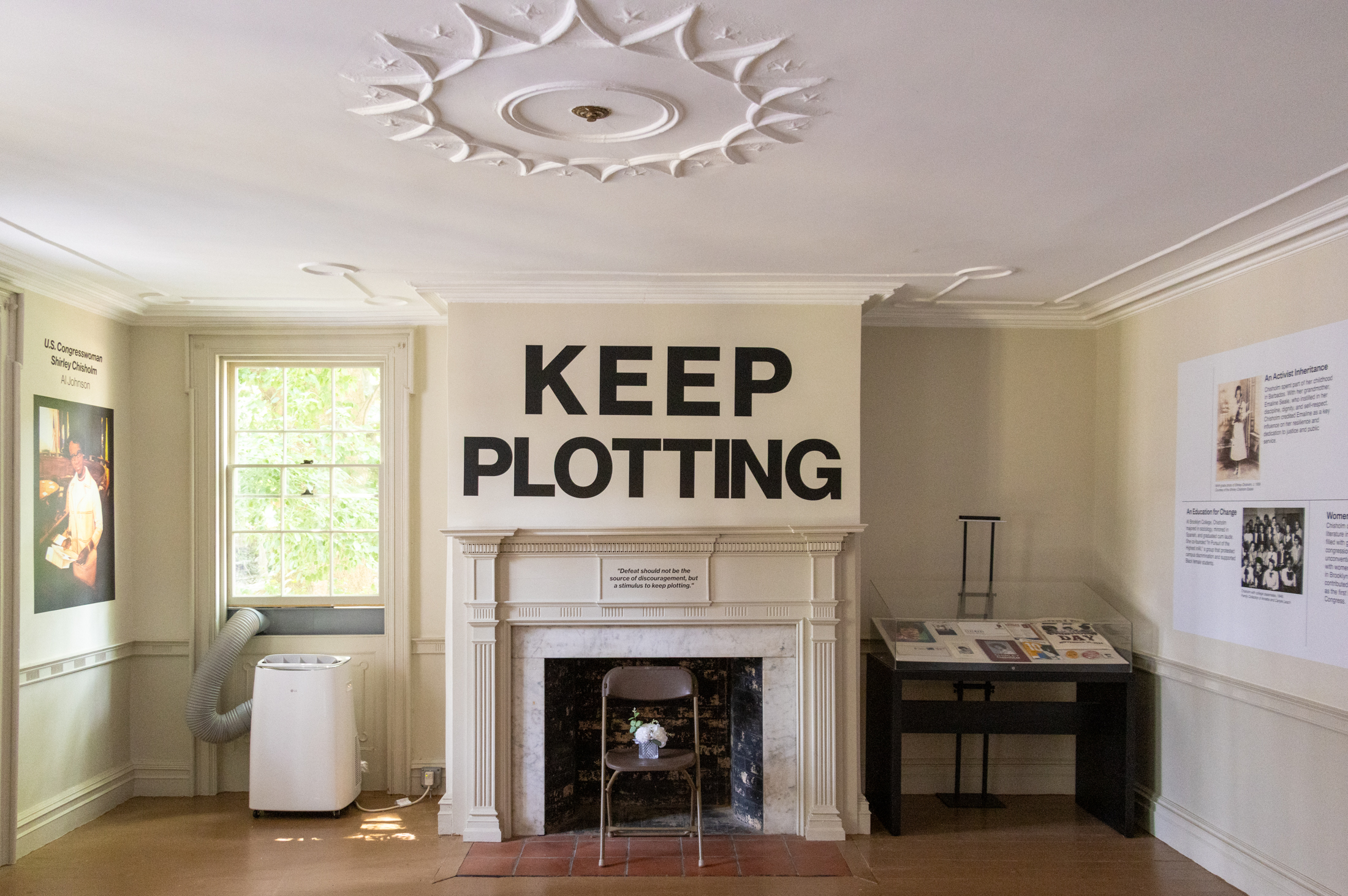 parlor with a mantel with the words "keep plotting" on the wall