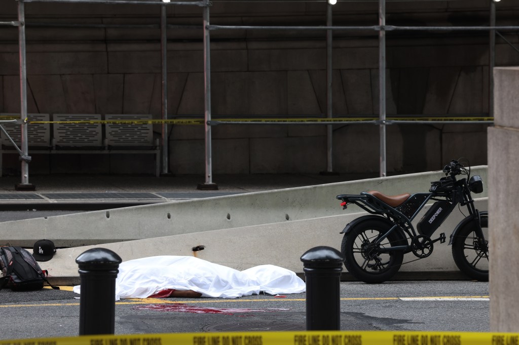 A body covered in a white sheet with blood on the ground next to an e-bike, behind a yellow "FIRE LINE DO NOT CROSS" tape.