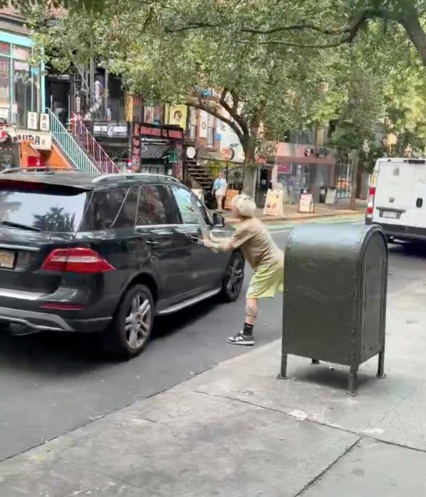 A still from a video showing a man smashing a skateboard against a car.