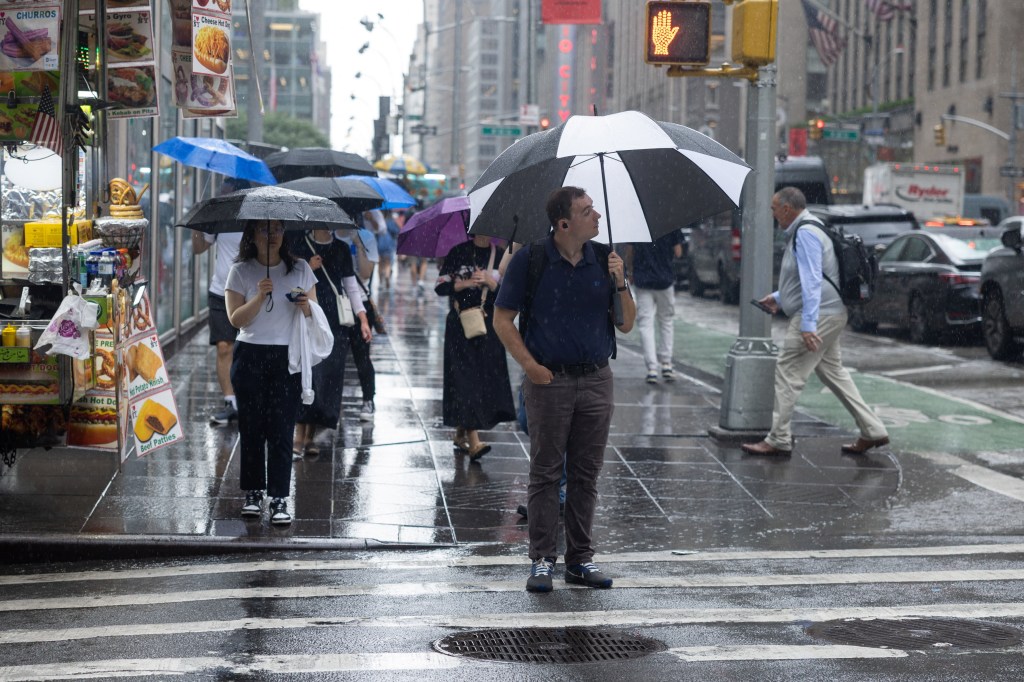 A man waits to cross the street during a rain storm in New York City, U.S., July 21, 2026. REUTERS/Jordan Tovin