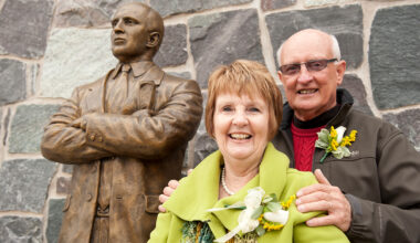 Jill and Terry Martin stand in front of the Terry Martin statue at the entrance of Roos House.