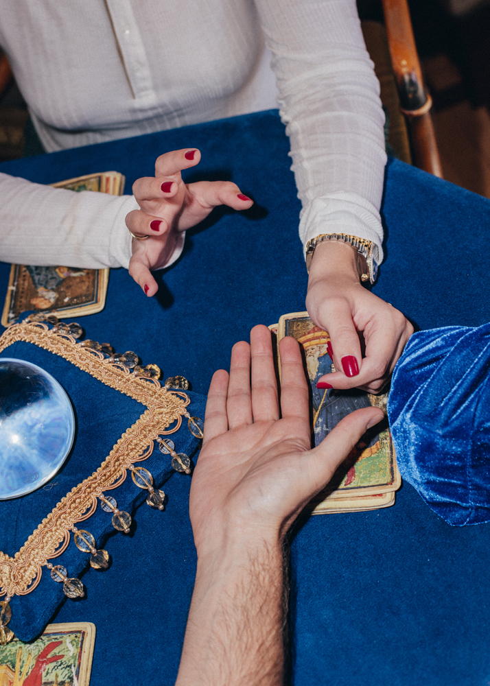 Hands with red nail polish during a palm reading session over tarot cards on a blue cloth with gold trim.