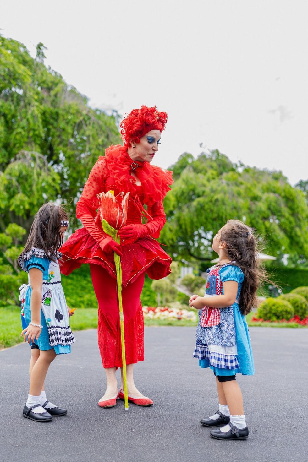 Performer in red Alice in Wonderland Red Queen costume interacts with two children in costumes outdoors at NYBG