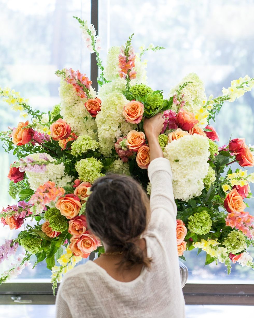 Person arranging colorful flowers in a large bouquet by a window at NYBG