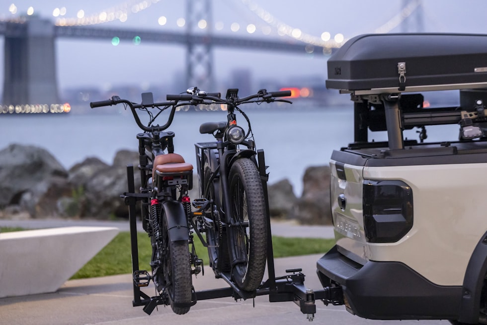 Electric bikes on a truck hitch rack near a bridge.