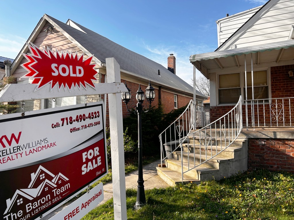 A realtor sign with "SOLD" in a red starburst shape stands in front of a recently sold home in Queens, New York.