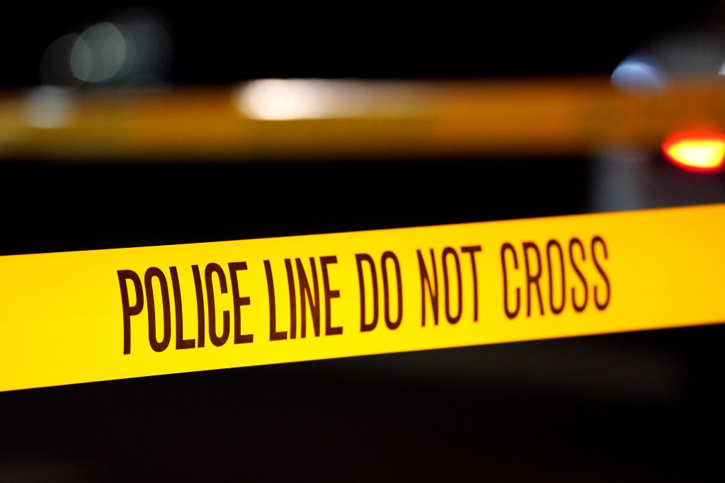 Yellow police tape at night with "POLICE LINE DO NOT CROSS" printed in black, illuminated by a red light in the background.