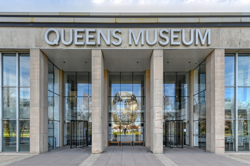 The Unisphere sculpture is visible through the front entrance of the Queens Art Museum in Fushing Meadows Corona Park.
