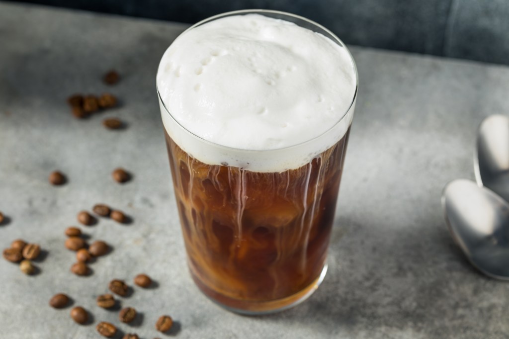Refreshing cold foam cold brew coffee in a glass, with coffee beans scattered around.