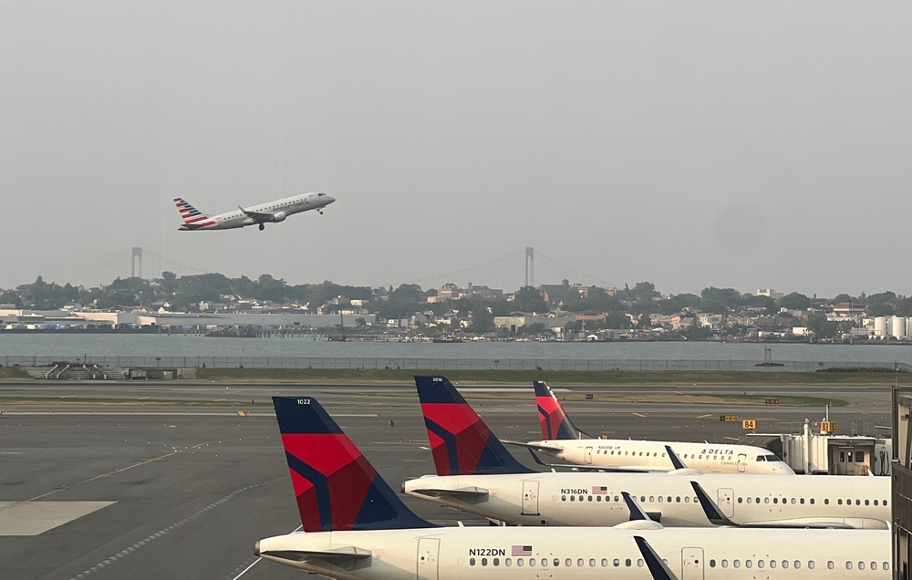 LaGuardia Airport runway with an American Airlines plane taking off and several delta planes waiting on a runway