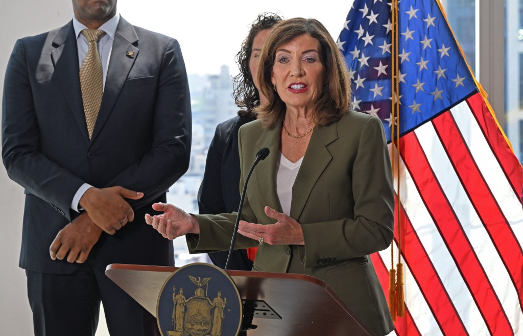 Governor Kathy Hochul at a podium speaking, with a US flag behind her.
