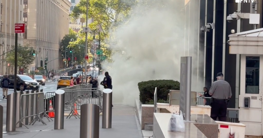 A street scene with white smoke billowing from an incendiary device thrown at 26 Federal Plaza.