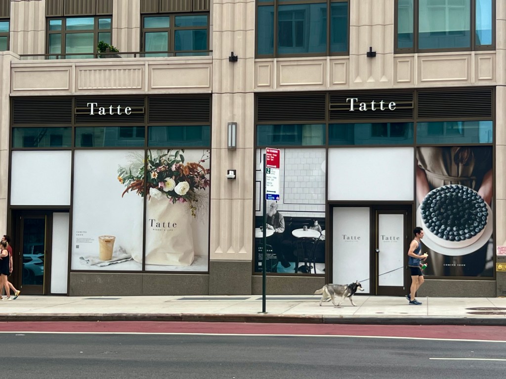The exterior of Tatte Bakery & Cafe on the Upper East Side, featuring window displays of floral arrangements, a coffee, and a blueberry tart.