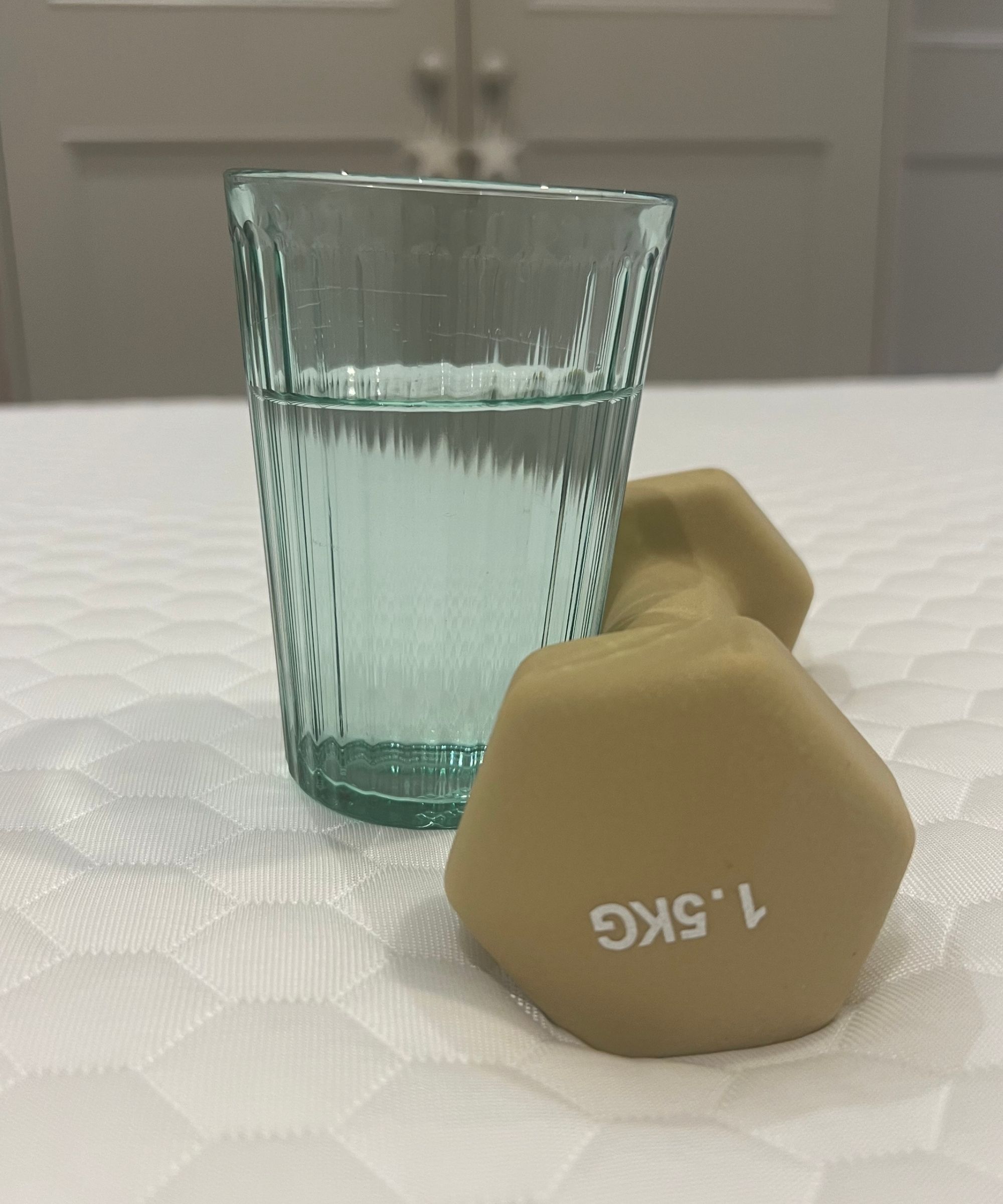 Testing the motion isolation of the Brooklyn Bedding Microcoil mattress topper with a light green glass of water and beige 1.5 kg weight