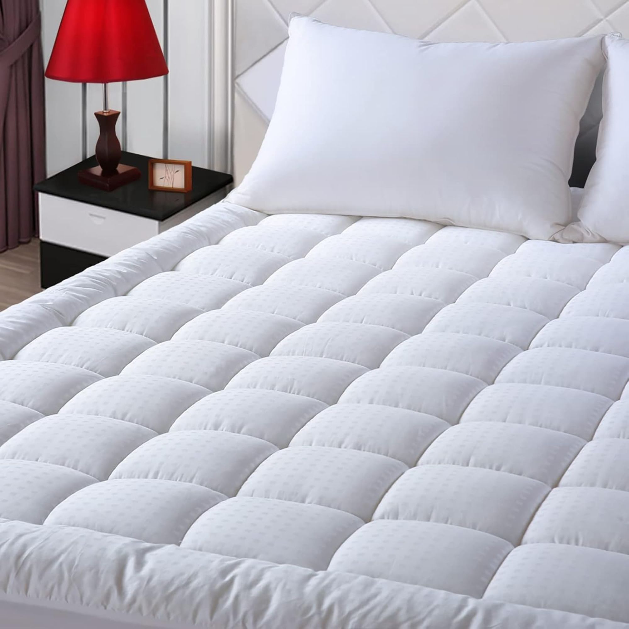 White EASELAND Mattress Pad with white pillows on a bed beside a black and white bedside table with lamp with red lampshade.