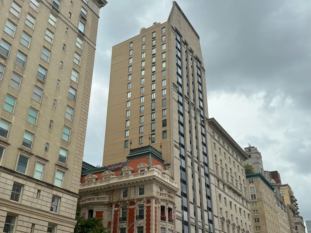 A street view showcasing a mix of tall buildings, including a modern high-rise and a historic structure with ornate detailing, set against a cloudy sky.
