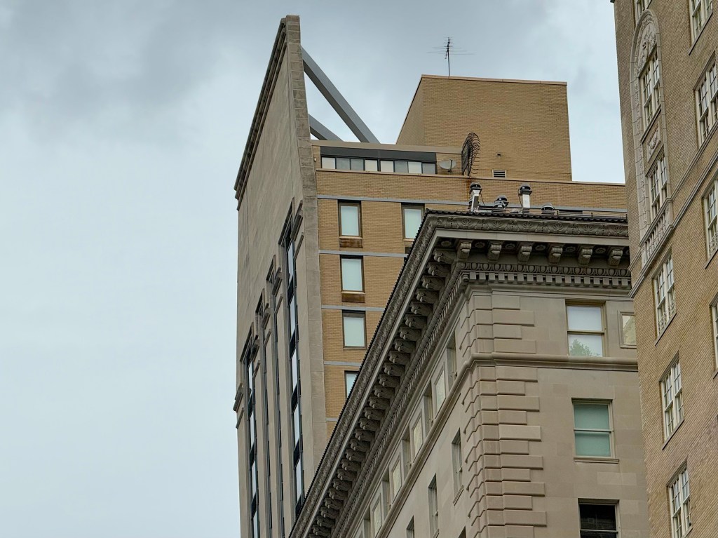 View of two buildings featuring a modern structure with a sharp roofline and a historic facade, set against a cloudy sky.