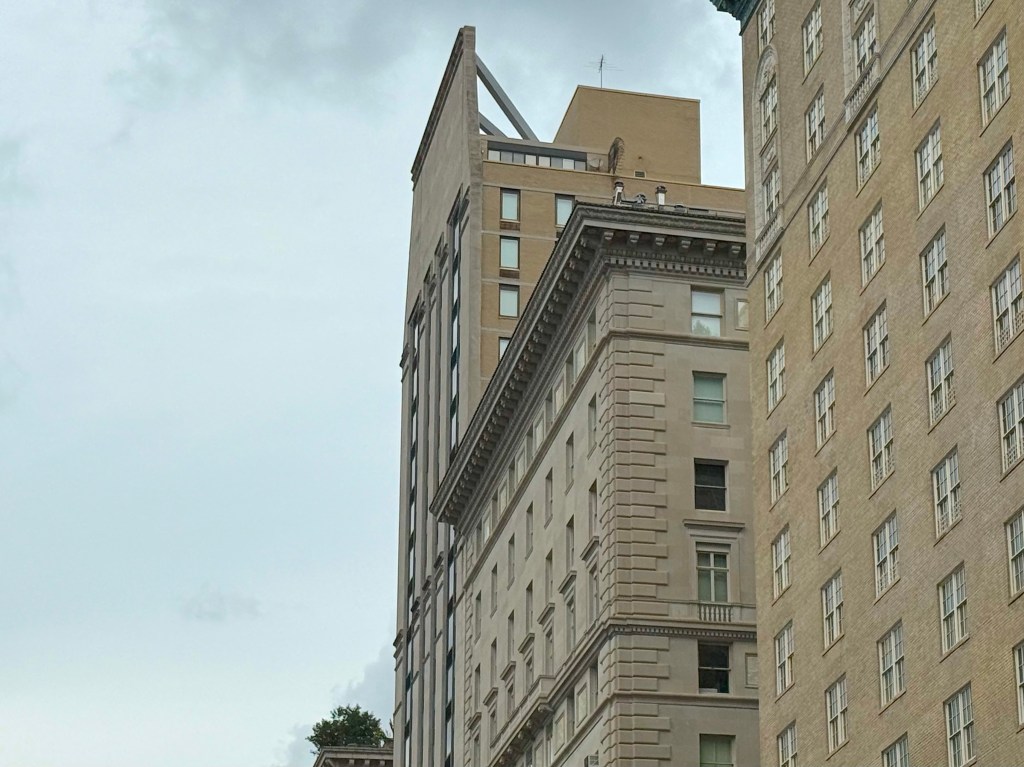 A view of two buildings in an urban area, showcasing distinct architectural styles, with a cloudy sky in the background.