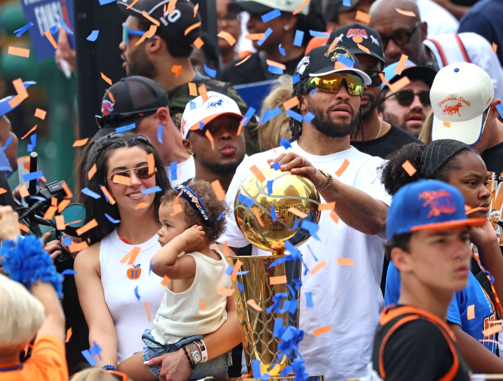 New York Knicks guard Jalen Brunson with his wife and child, holding the Championship trophy at a ticker-tape parade.