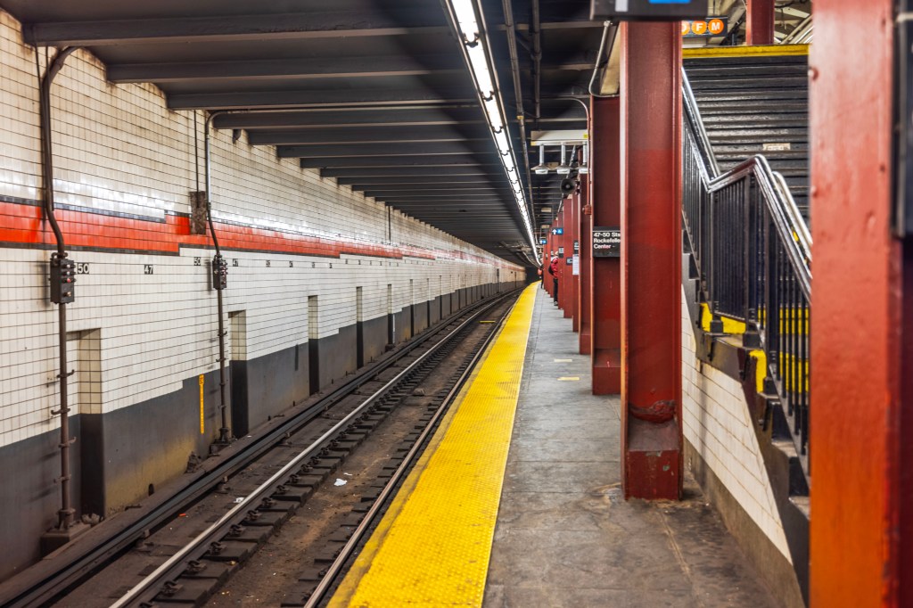 Empty subway platform at 47-50 Streets Rockefeller Center station in New York with tiled walls and tracks.