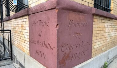 A brick building corner with an engraved stone featuring text that reads