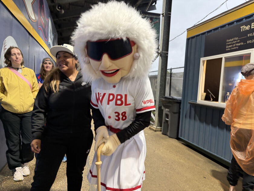 A fan poses next to a mascot of 99-year-old Maybelle Blair at the Women's Professional Baseball League Inaugural game Saturday in Springfield. Blair played for the iconic Rockford Peaches professional women’s baseball team in the 1940s and ‘50s, which was famously depicted in the 1992 film, “A League of their Own.”