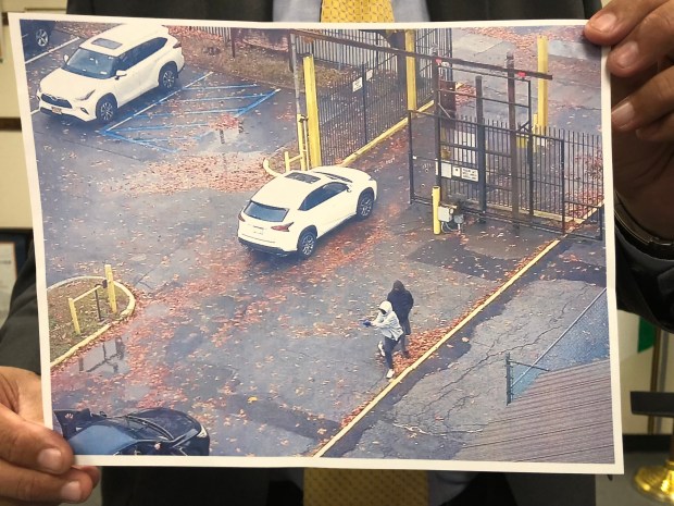 In a still from video, two perpetrators, one of whom pulls a gun, as cops in unmarked black car (lower left) enter a parking lot behind the Stevenson Common at 755 White Plains Road in the Bronx on Nov. 22, 2024. (NYPD) 