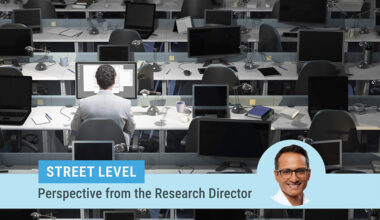 Street level column by Research Director Kartik Athreya. Image of Athreya on top of a photo of a large room with rows of desks and laptops with only one man sitting at one desk working.