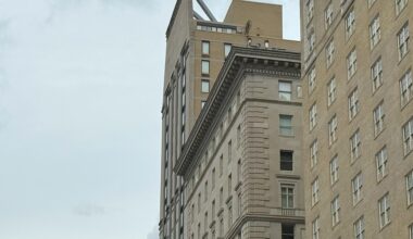 A view of two buildings in an urban area, showcasing distinct architectural styles, with a cloudy sky in the background.