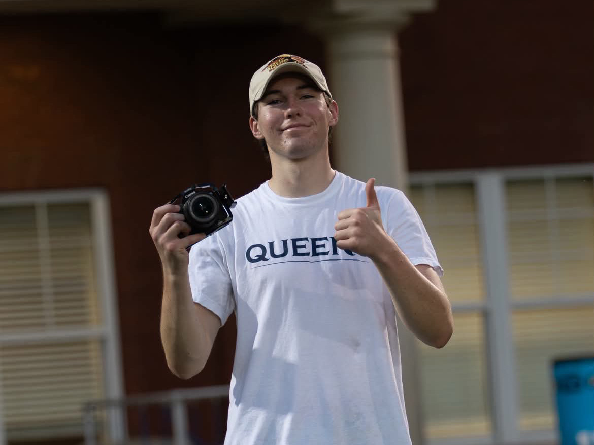 A smiling man with white baseball cap and teeshirt that says