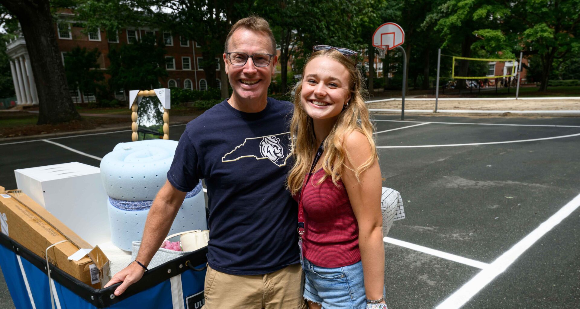 man with navy blue Queens University teeshirt on stands with girl with long blond hair wearing shorts and a maroon tank top.