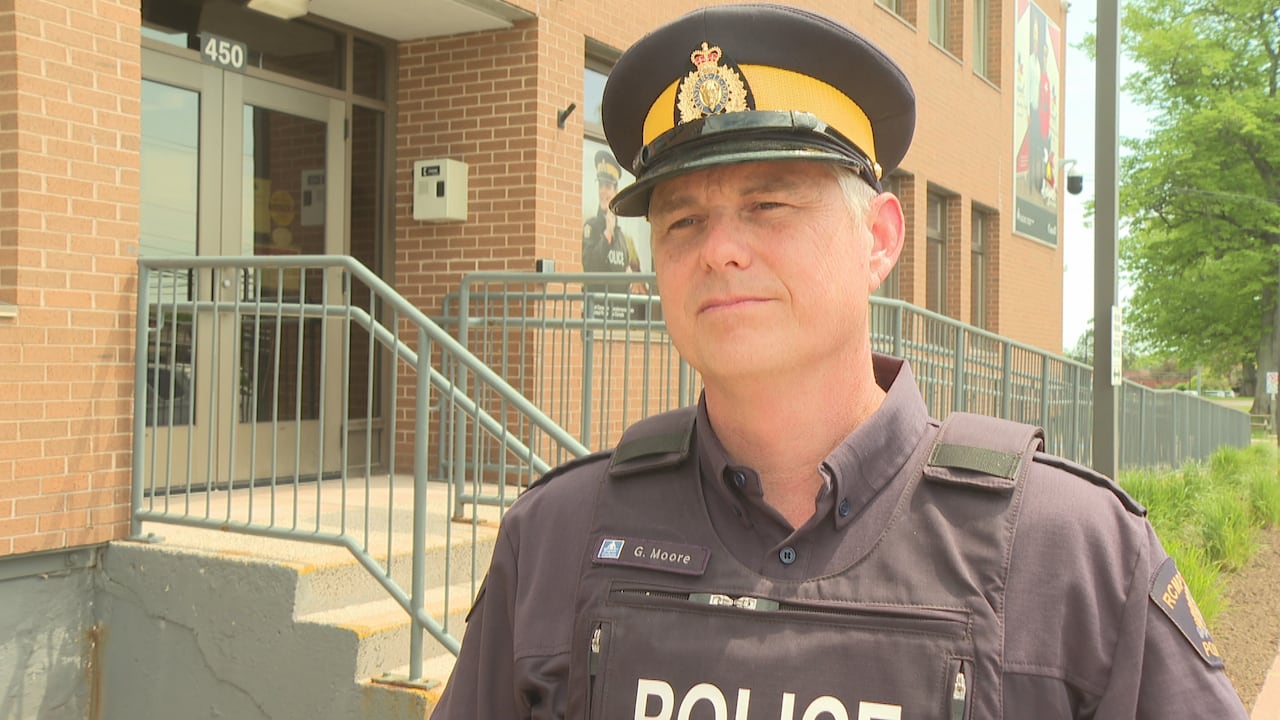 An officer wearing a Royal Canadian Mounted Police (RCMP) uniform stands outside a brick police detachment building.