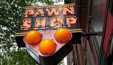 An upward view of a neon sign reading “Pawn Shop” attached to a wooden panel on the side of a building.
