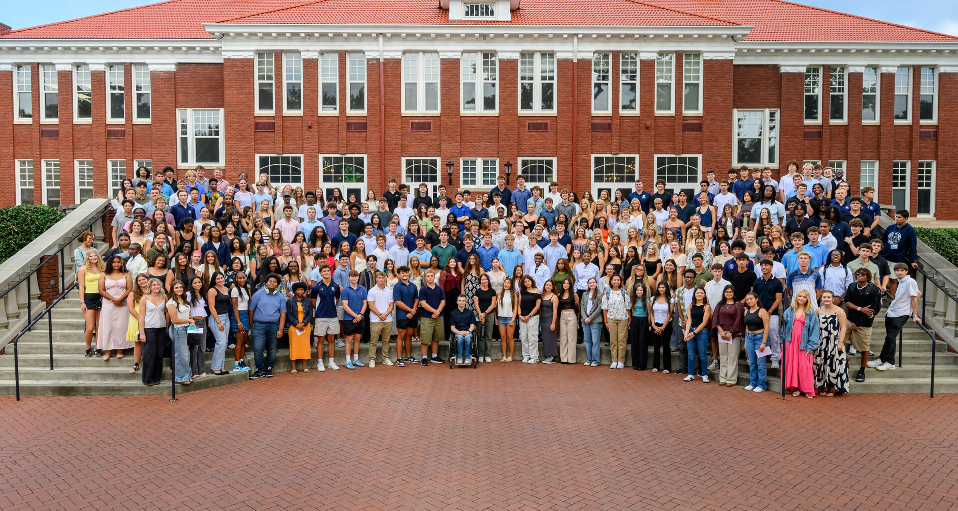 More than 300 Queens University students gather at the steps of Hall Brown Terrace in front of a red brick building known as Queens Hall.