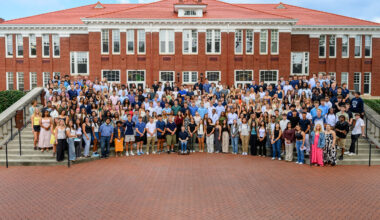 More than 300 Queens University students gather at the steps of Hall Brown Terrace in front of a red brick building known as Queens Hall.