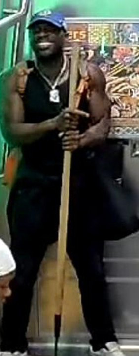 Suspect in a blue baseball cap and black tank top holding a gardening tool.
