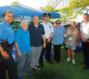 Greeting the park goers (l. to r.): Community Affairs PO Rosemary Wanzer; Joe DiPietro, the President of the Federation of Italian American Organizations of Queens (FIAOQ) which co-sponsored the event; Ted Psahos, President, 114th Precinct Community Council; Inspector Seth Lynch, Commanding Officer of the 114th Precinct; Angie Markham, Executive Director of the FIAOQ; event coordinator Diana Turek; and George Rivera, Vice President of the 114th Precinct Community Council. Photos by Walter Karling