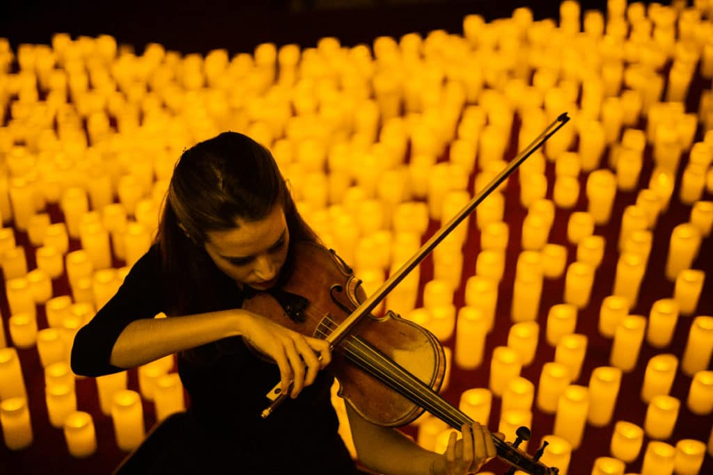 A woman playing the violin with candles behind her.
