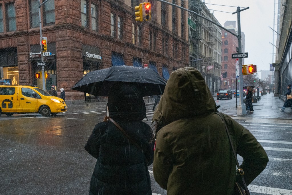 Two people walk through lower Manhattan as it snows.
