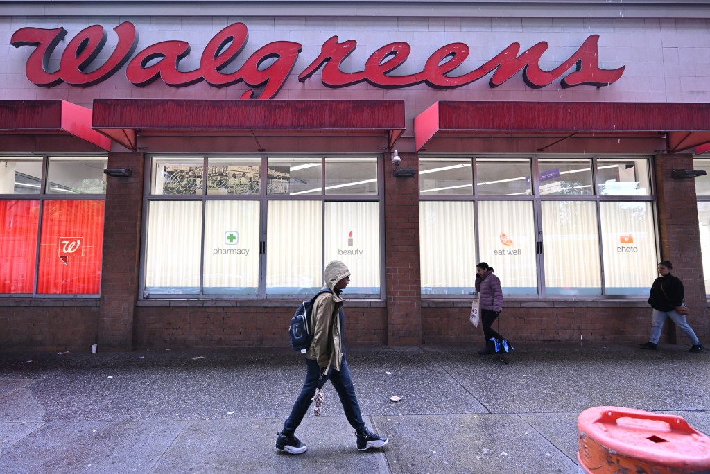 Exterior of a Walgreens store with three people walking on the sidewalk in front of it.