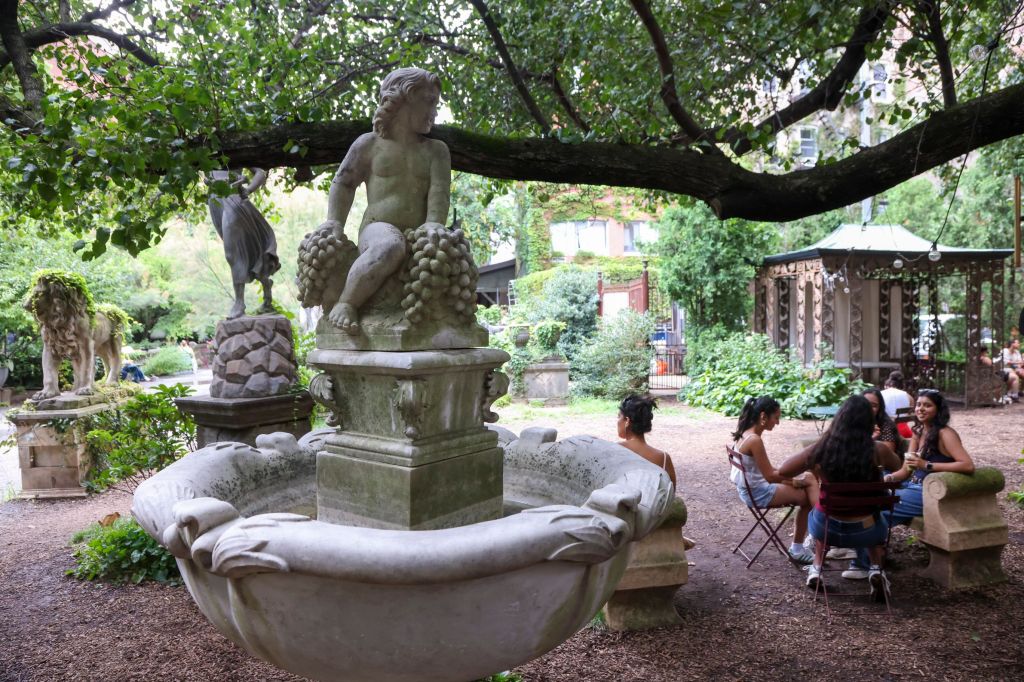 People sitting near a fountain with statues in Elizabeth Street Garden.