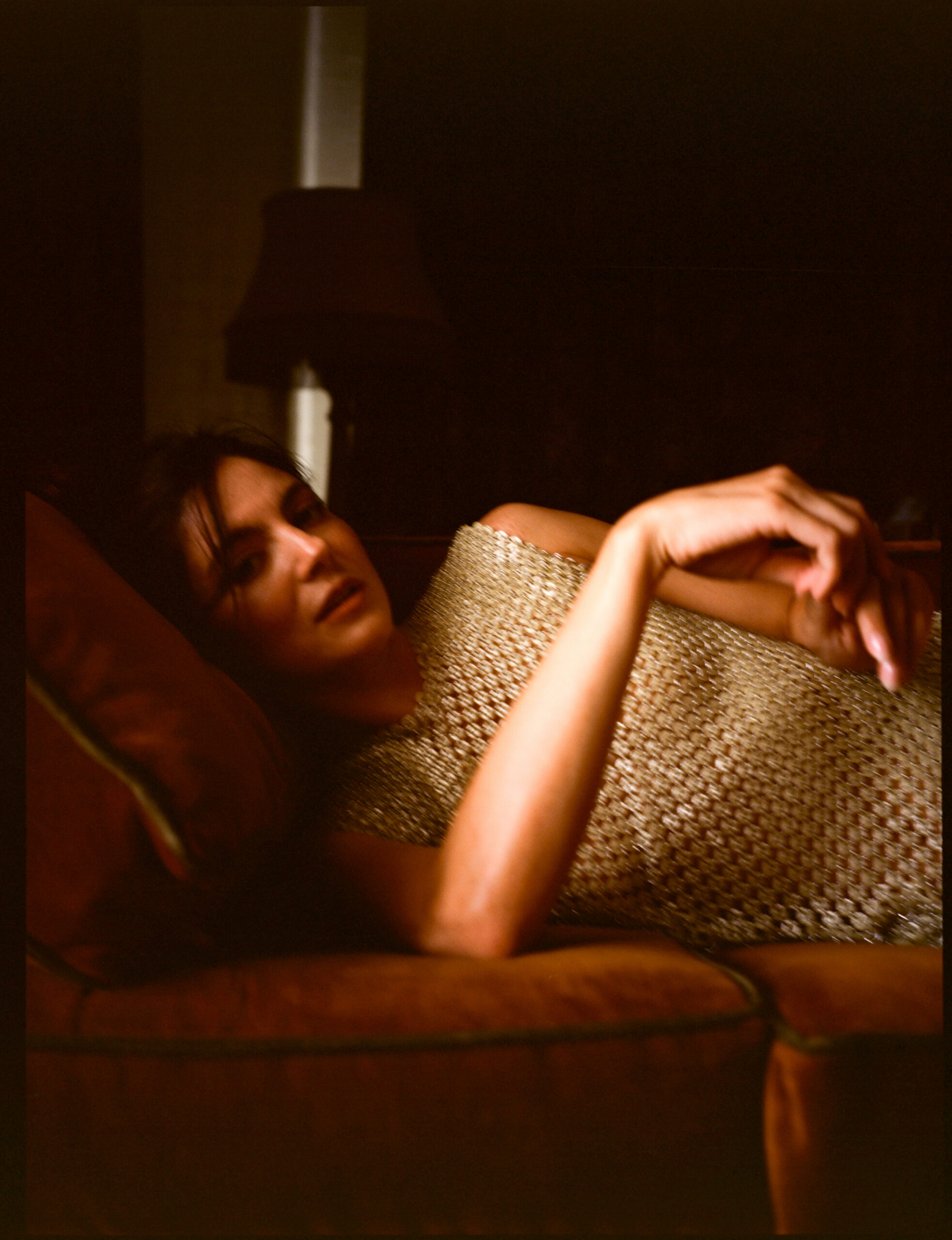Monica Barbaro lying on a red velvet couch