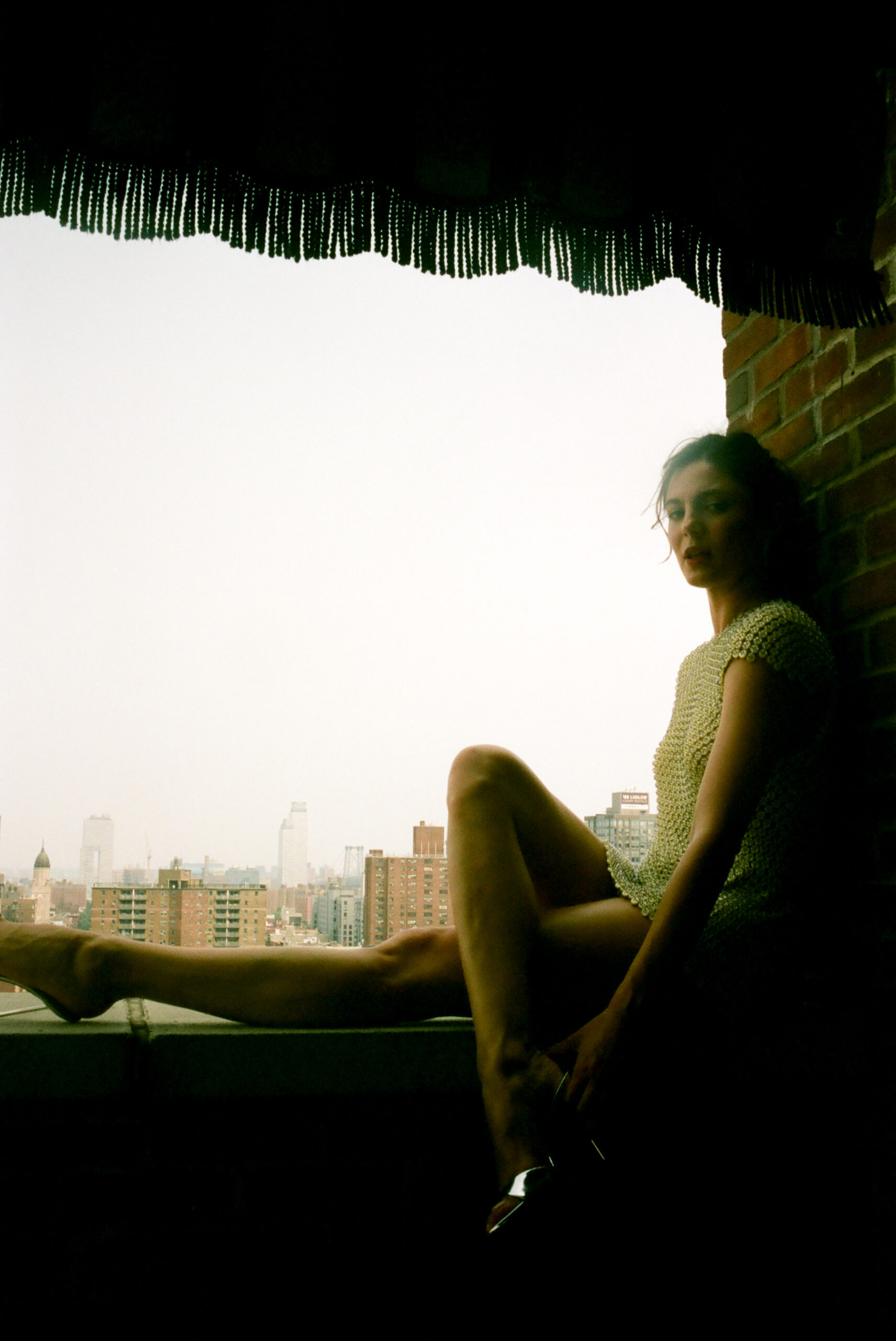 Monica Barbaro sitting on the ledge of a balcony