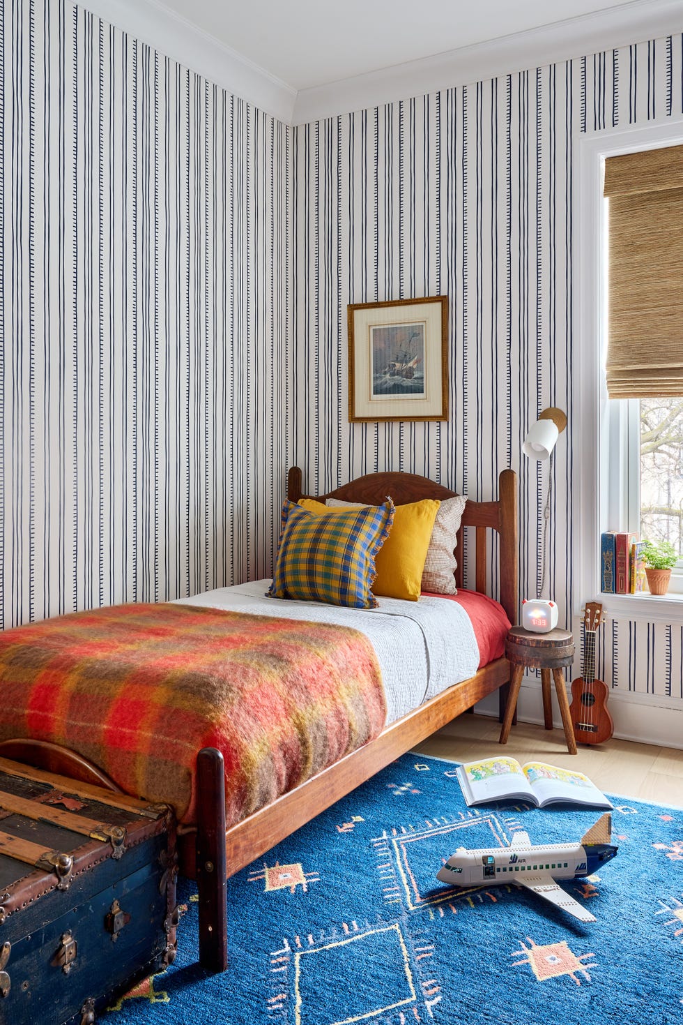 Cozy bedroom featuring a bed with colorful pillows, a patterned rug, and decorative items like a guitar and books.