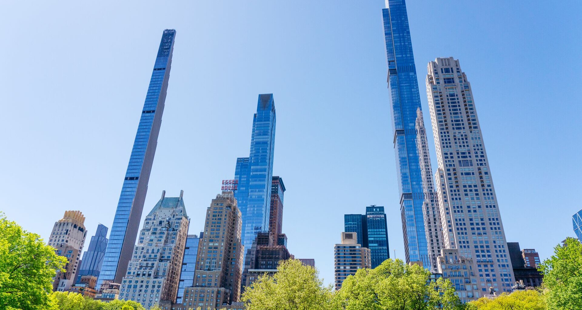 View of Midtown Manhattan skyscrapers rising above the trees of Central Park on a clear day.