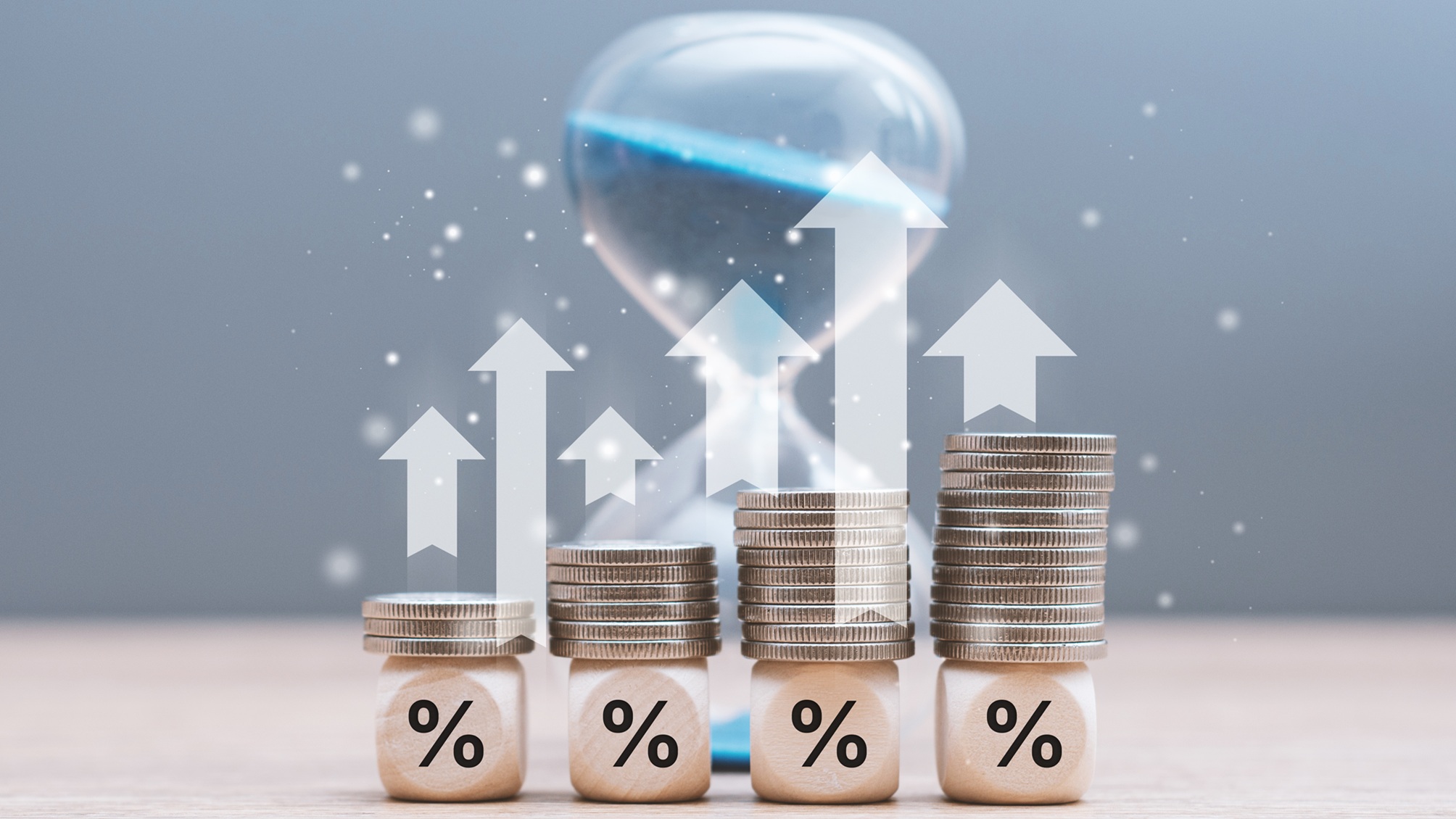 Stacked coins arranged in increasing height on cubes with percent symbols and up arrows in front of an hourglass.